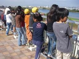 屋上にて庭窪浄水場の概要や取水口について、小学生達が解説を聞いている様子の写真