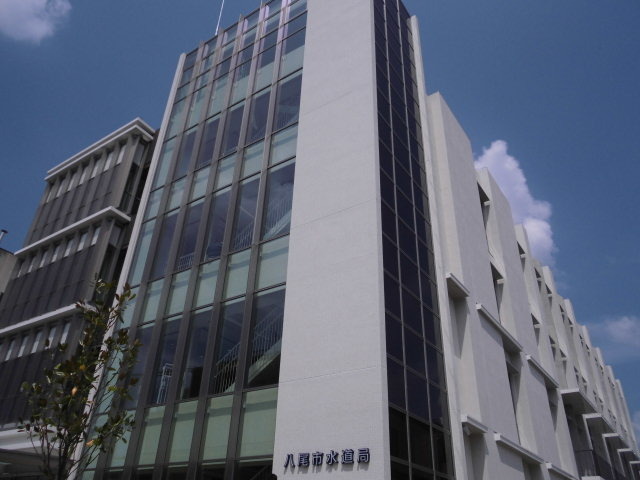 外壁が白色で「八尾市水道局」のロゴのある面がガラス張りになっている建物外観を写した写真