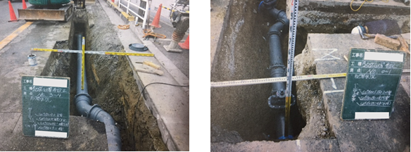 道路が彫られ、地中にある水道管が見える状態になっている、周りには赤いポールが立てられ、高さを測る工事用の計量器が見えている写真