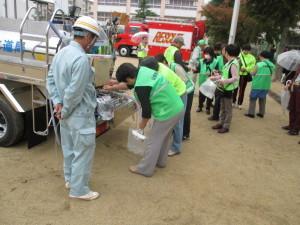 給水車から水を汲むために並んでいる人々の写真