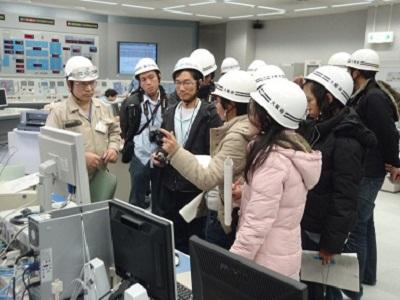 ヘルメットをかぶった海外研修生と職員たちが、モニターの前に集まっている写真