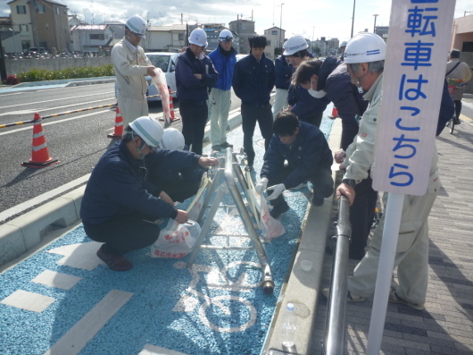 3名の男性が非常用給水スタンドから飲料水袋へ給水をしている様子を関係者の人たちが確認している写真