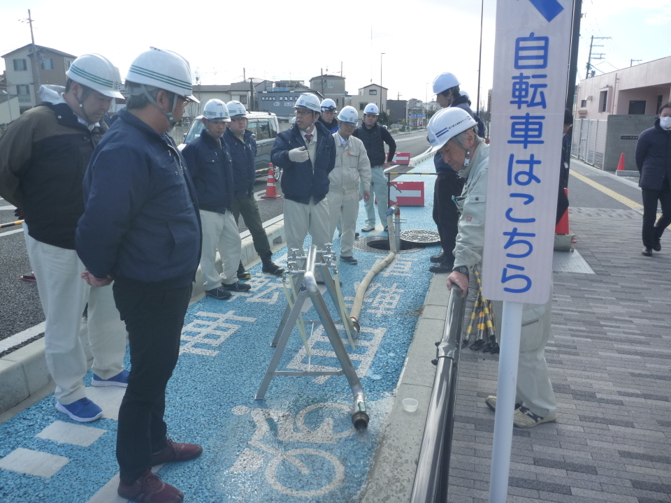 たくさんの関係者の人たちがヘルメットを着用しながらマンホールから非常用給水スタンドへ給水している様子を確認している写真