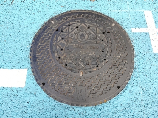 広域水道 あんしん給水栓と書かれ、中央に消防車の様なイラストが描かれたマンホールの蓋の写真
